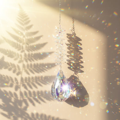 Attrape-soleil Andromaque One2K – pendentif larme en cristal K9 effet AB transparent avec spirale irisée, reflets arc-en-ciel sur fond sable doré
