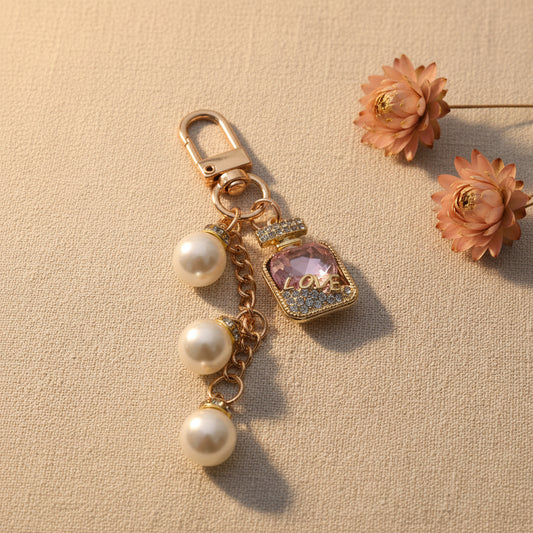 Bijou de sac téléphone 3-en-1 Élixir Rose One2K – photo ambiance sur tissu beige avec fleurs séchées roses et terracotta, flacon strass doré cristal rose LOVE et perles nacrées
