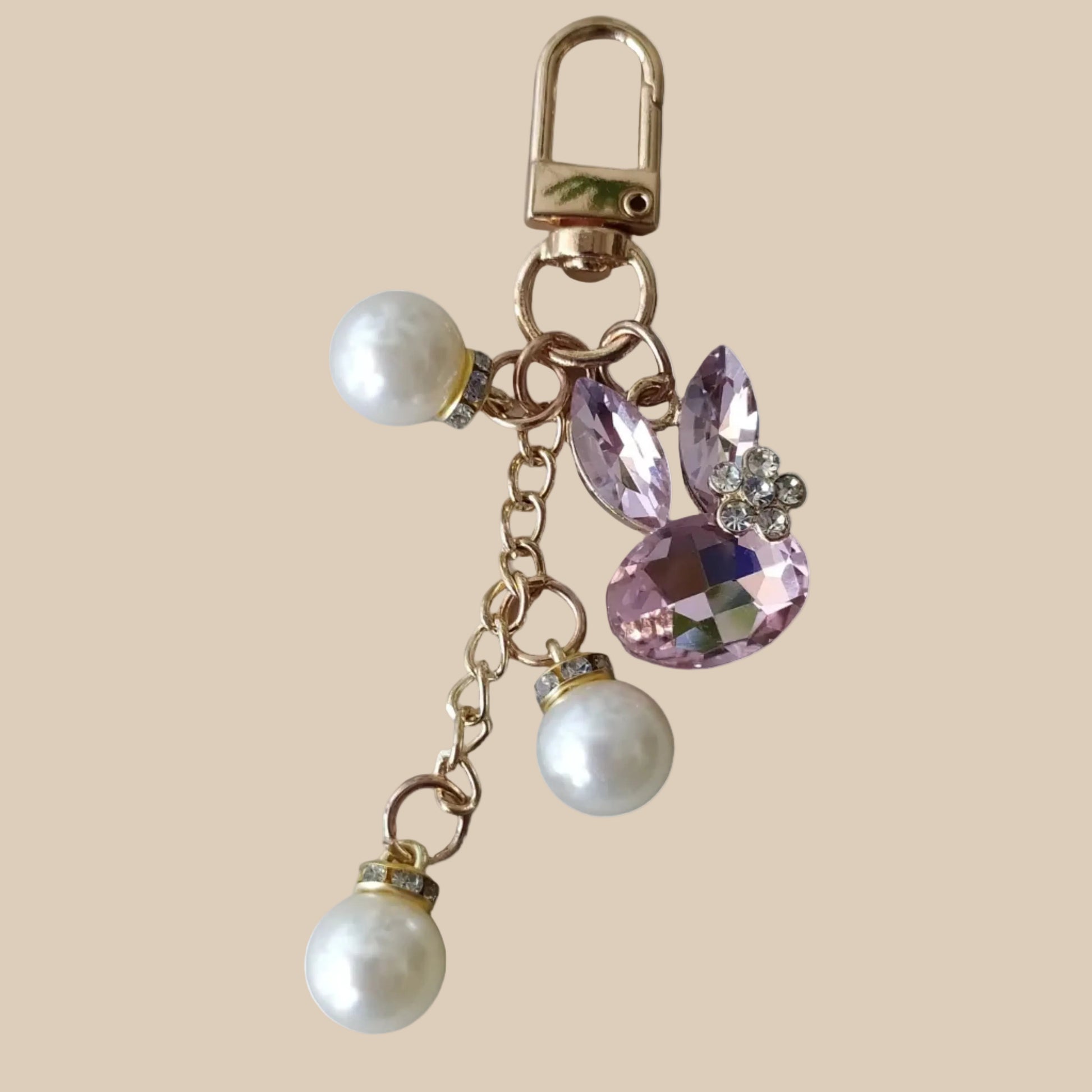 Bijou de sac téléphone 3-en-1 Lapin de Cristal One2K – vue présentation sur fond sable, lapin formé de cristaux rose taille marquise et ovale, strass transparents, perles nacrées blanches et mousqueton doré
