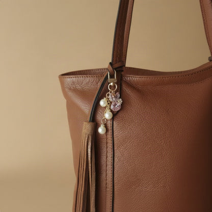 Bijou de sac téléphone 3-en-1 Lapin de Cristal One2K – situation d'usage accroché à un grand sac cabas en cuir camel avec pompon, lapin cristal rose et perles nacrées
