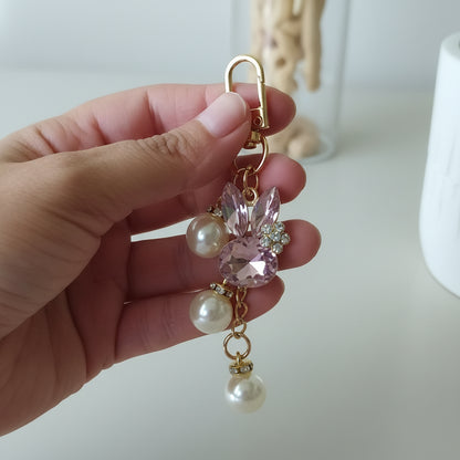 Bijou de sac téléphone 3-en-1 Lapin de Cristal One2K – photo dimensions tenu en main devant un pot blanc avec cactus, lapin cristal rose, perles nacrées et mousqueton doré
