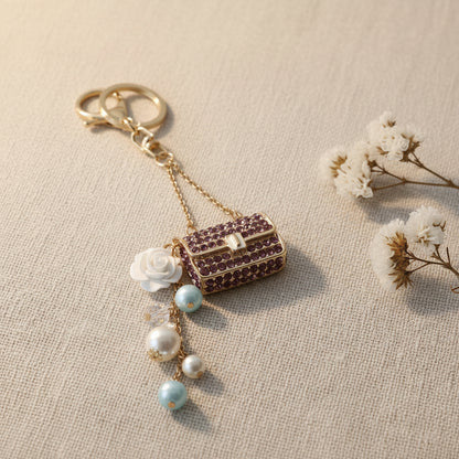 Bijou de sac téléphone 3-en-1 Mini Sac Pourpre One2K – photo ambiance sur tissu beige avec fleurs séchées blanches, mini sac strass pourpre et perles bleues et nacrées