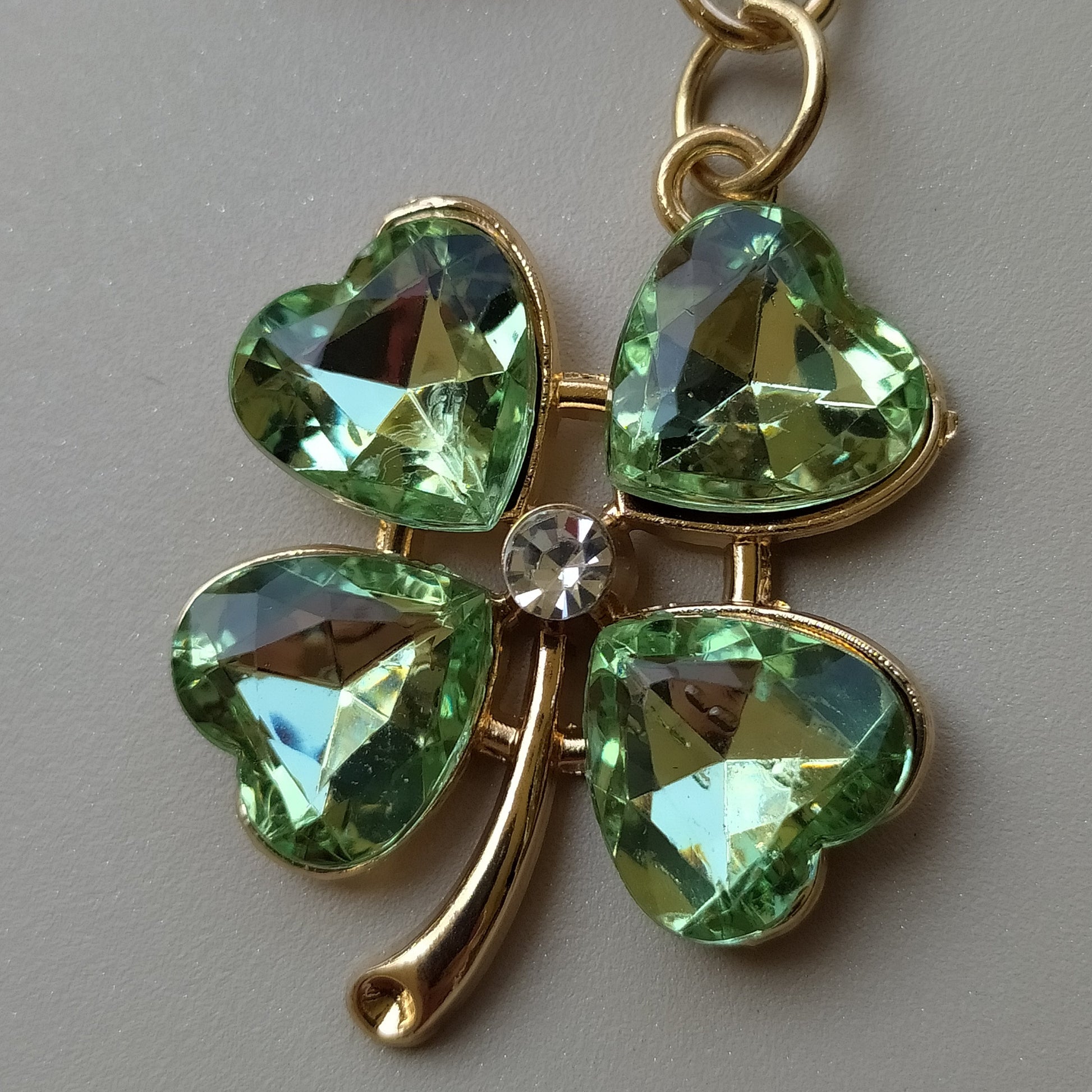 bijou de sac et de telephone 3 en 1 trèfle émeraude One2K gros plan sur fond beige cristal vert avec un cristal blanc au centre du trèfle contour doré