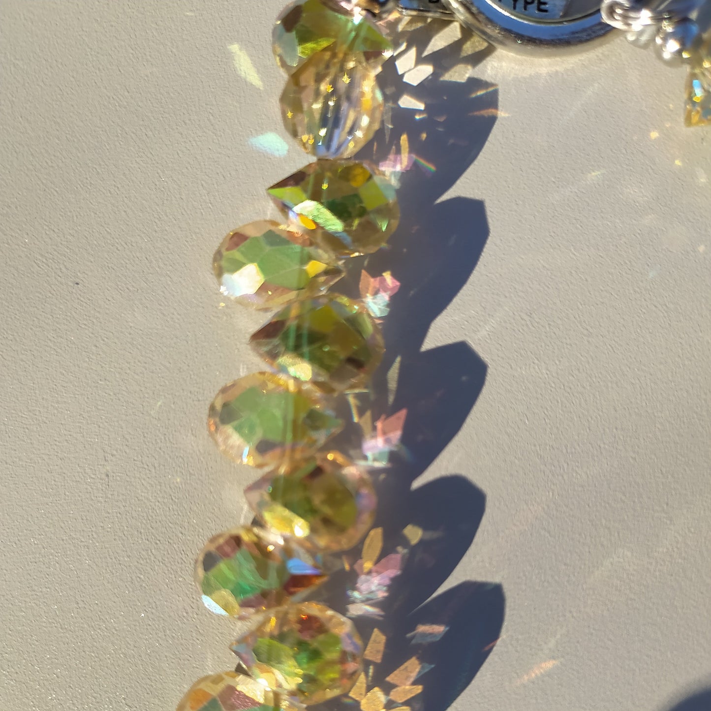 Bijou 2-en-1 Dragonne de Poignet & Bijou de Sac Éclat Boréal reflets solaires One2K – gros plan sur les perles de cristal facettées aux reflets dorés, verts et irisés solaires, anneau argenté visible en haut

