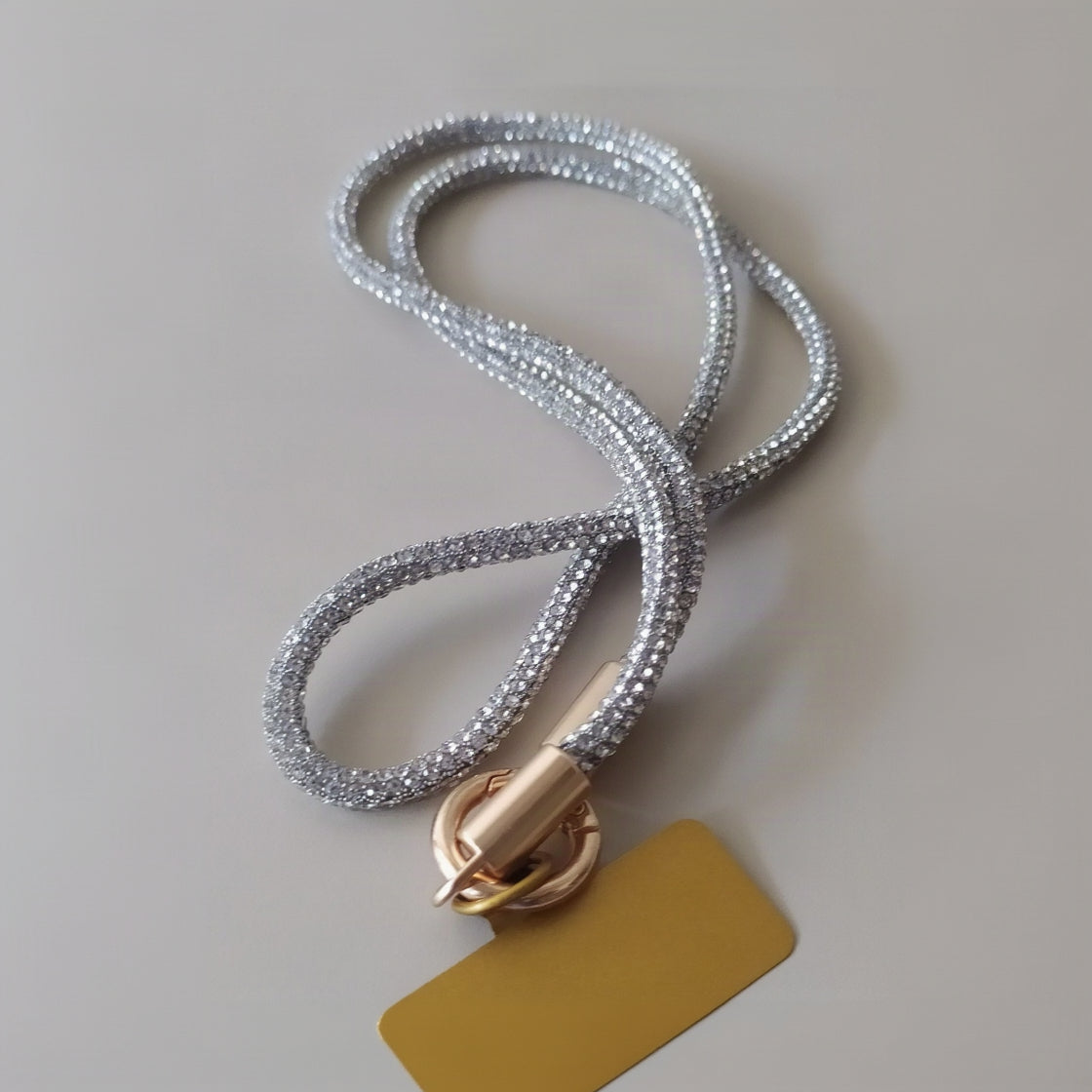 Collier téléphone infini strass One2K version argent – gros plan sur la corde tubulaire entièrement recouverte de micro-strass argentés scintillants, fermoir cylindrique doré et anneau ressort doré avec patch jaune

