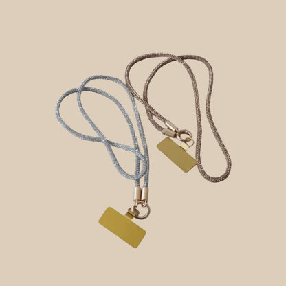 Collier téléphone infini strass One2K – vue présentation sur fond sable, duo de colliers téléphone en corde strass argentée et dorée champagne avec patch rectangulaire doré et mousqueton doré
