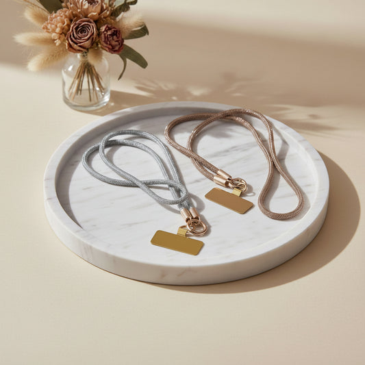 Collier téléphone infini strass One2K – photo ambiance sur plateau en marbre blanc fond beige ensoleillé avec vase de fleurs séchées, duo de colliers strass argenté et doré champagne avec patch rectangulaire doré
