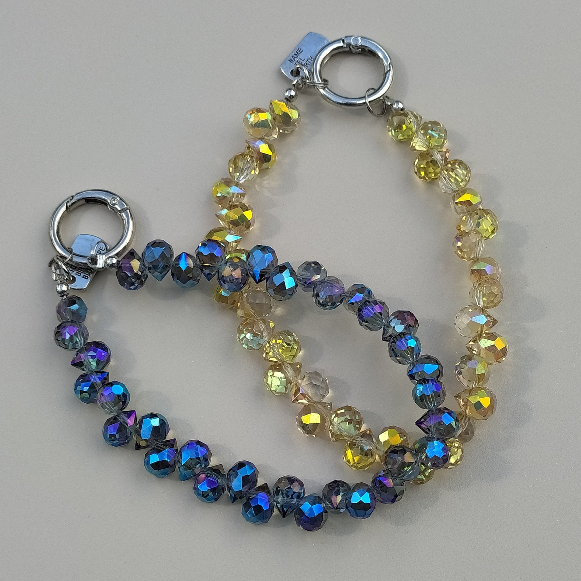 Bijoux de sac et de téléphone dragonne poignet Eclat Boréal reflets azur et reflets solaires | One2K , les 2 variantes en présentaion sur fond neutre, reflets AB bleu azur irisé et solaires ocre scintillant - attache mousqueton rond argent