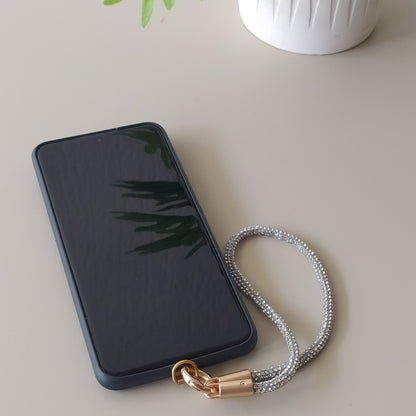 Dragonne poignet téléphone infini strass  One2K version argent – situation d'usage accroché à un smartphone noir sur fond beige, corde tubulaire strass argentée scintillante et fermoir doré
