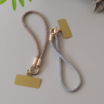 Dragonne poignet téléphone infini strass One2K – vue présentation sur fond gris, duo de dragonnes tubulaires recouvertes de micro-strass dorés champagne et argentés, fermoir cylindrique doré et patch rectangulaire doré
