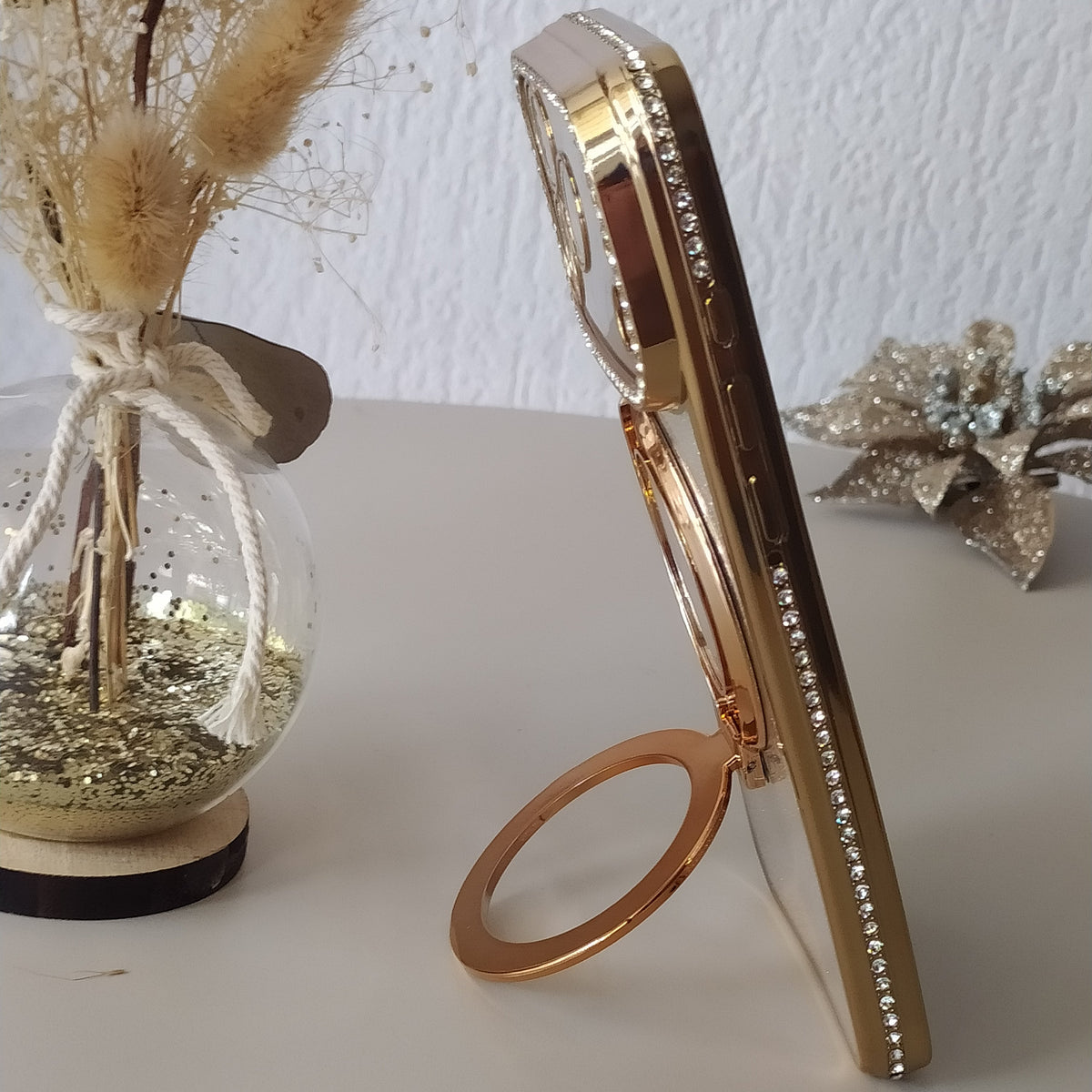 Coque iPhone 17 Pro Max Cristal Chic Or Solaire One2K – photo en situation, posé sur une table avec anneau support doré
